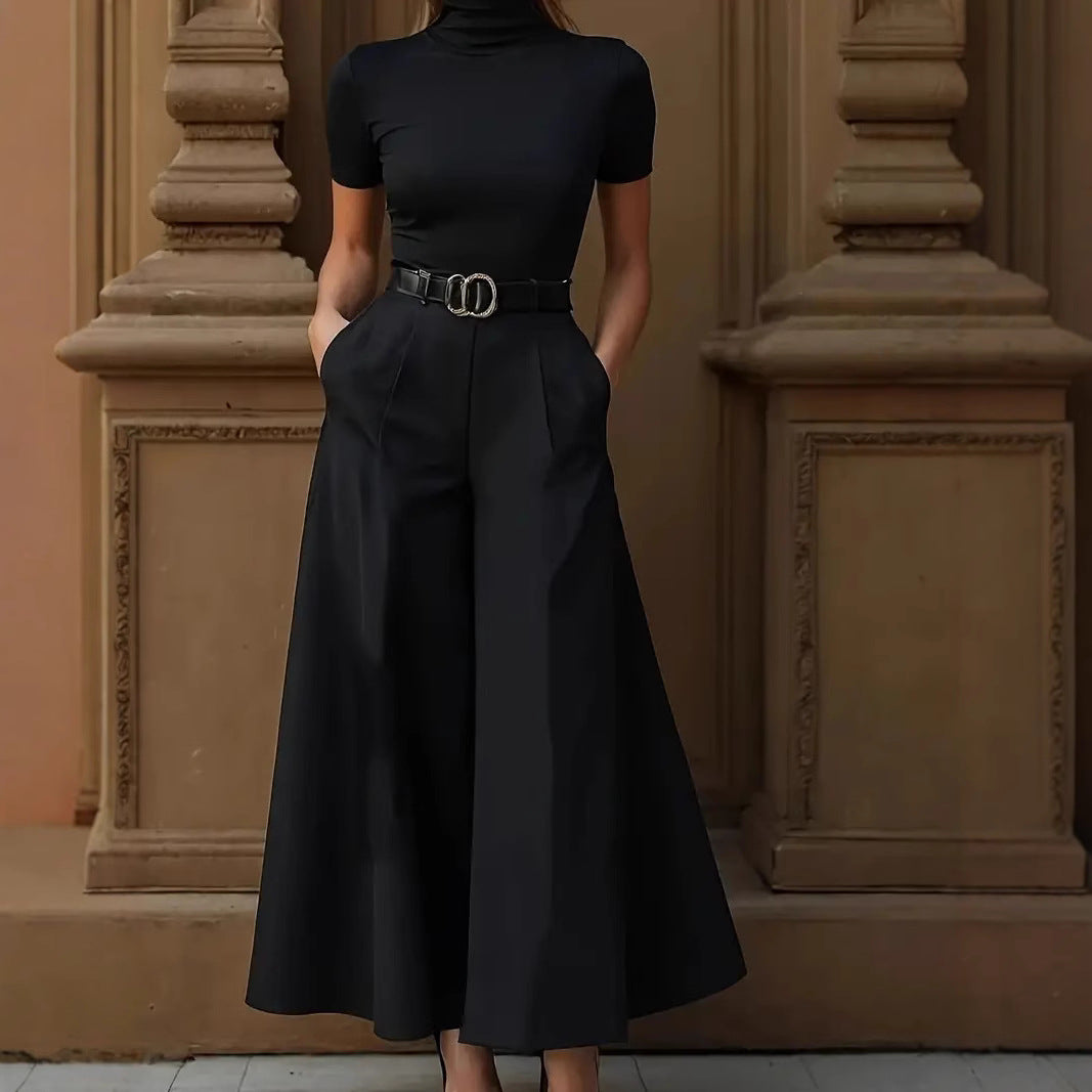 Person wearing a black dress with a belt in front of decorative columns.