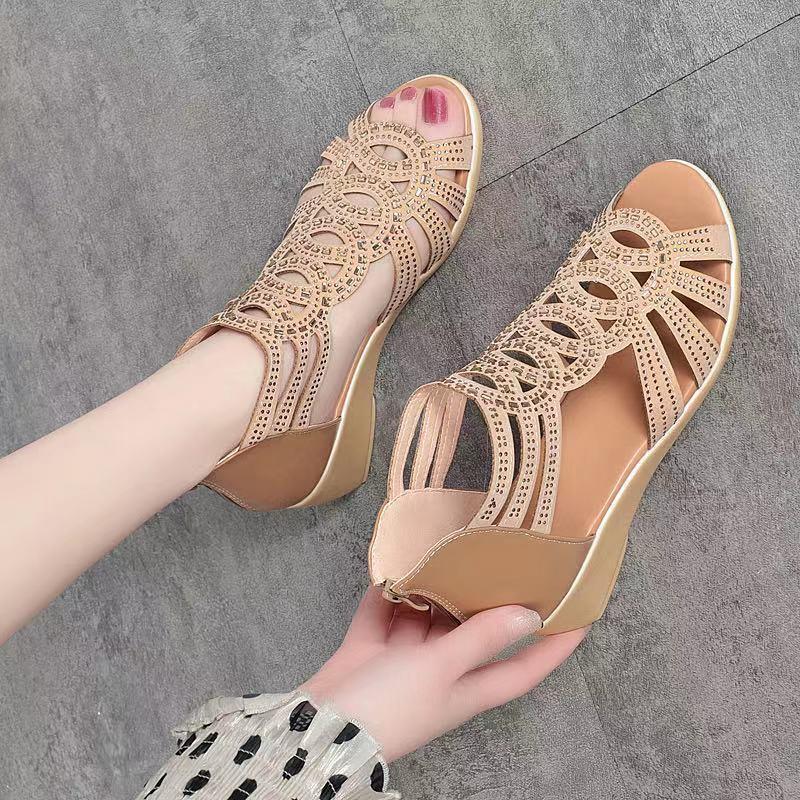 Beige open-toe sandals with detailed lace-up design worn by a person on a gray floor.