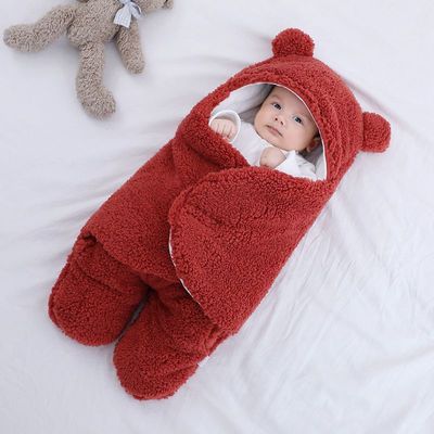 Baby in a red bear-shaped sleeping bag on a white surface with a plush toy.