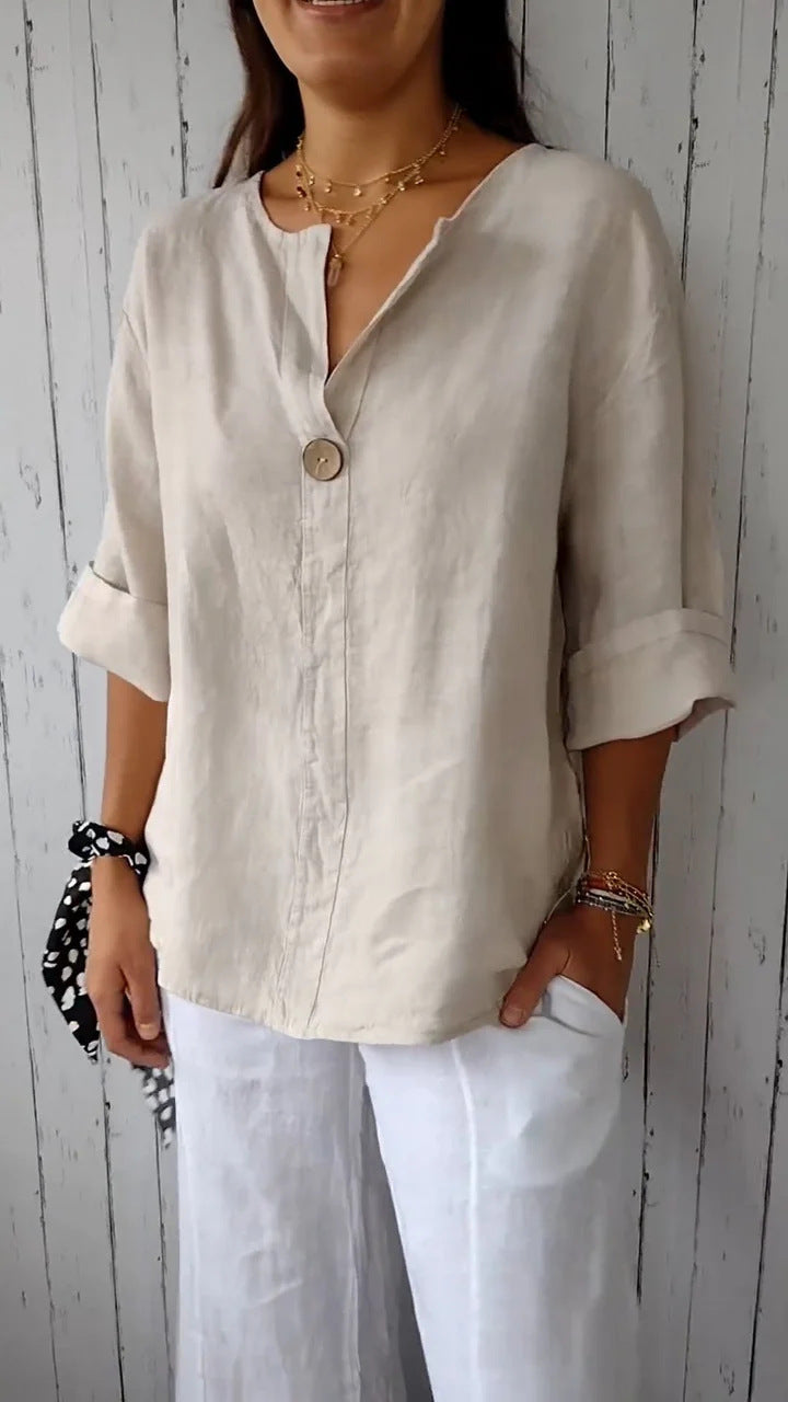 Woman wearing a beige button-up shirt and white pants against a wooden background