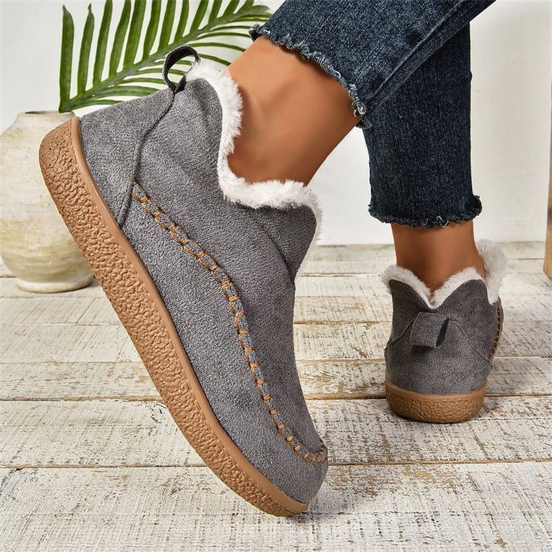 Gray slippers with brown soles worn by a person on a wooden floor.