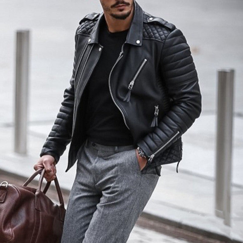 Man wearing a black quilted leather jacket and gray pants, holding a brown leather bag.