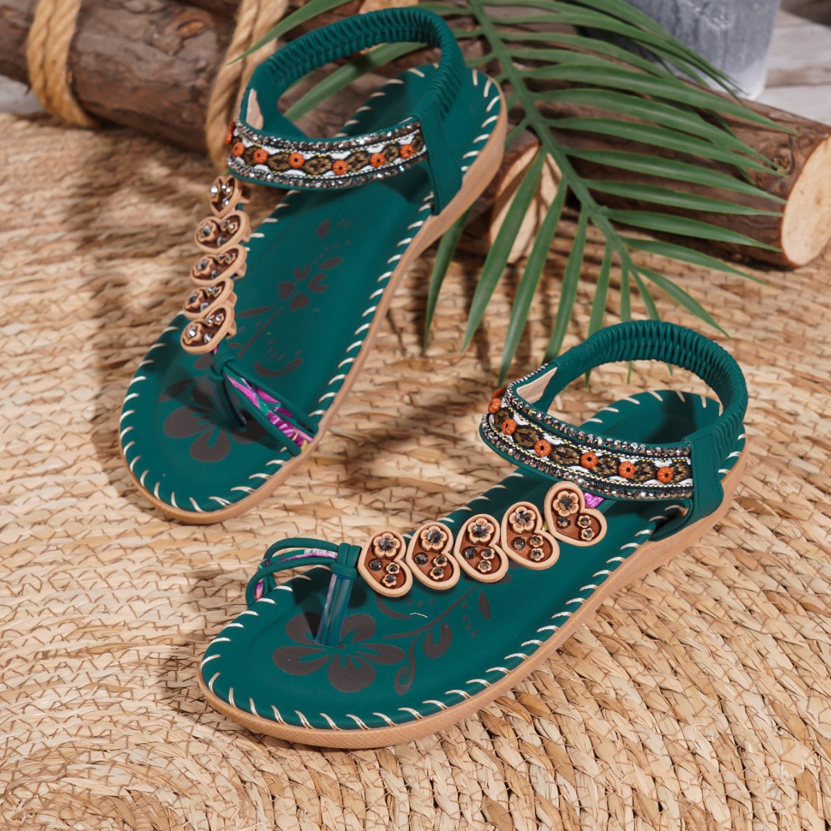 Teal sandals with decorative straps on a woven surface with leaves.