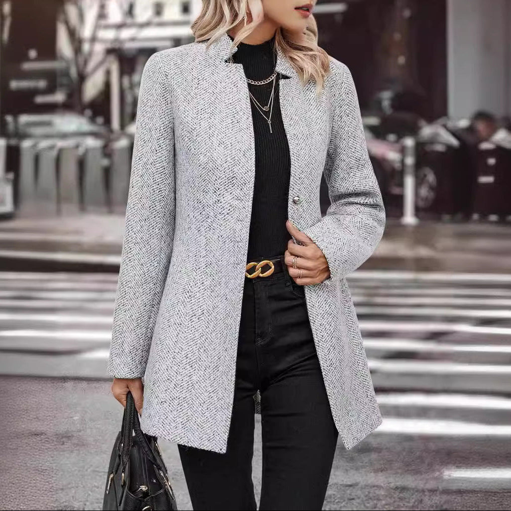 Person wearing a gray coat and black pants on a city street.