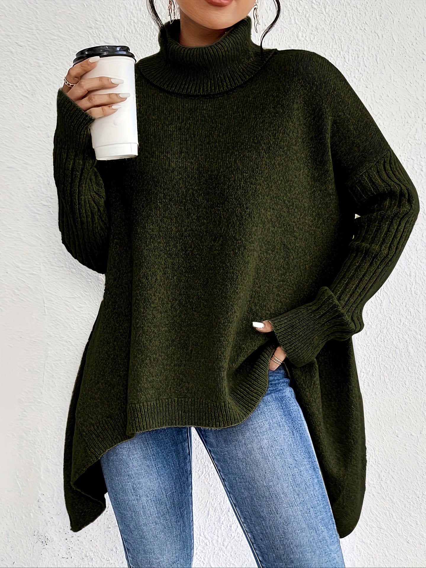 Person wearing a dark green sweater and blue jeans, holding a white cup with a black lid.