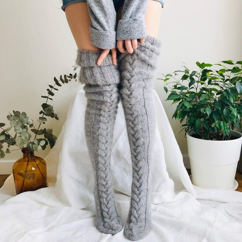 Person wearing gray knitted leg warmers standing indoors with plants in the background