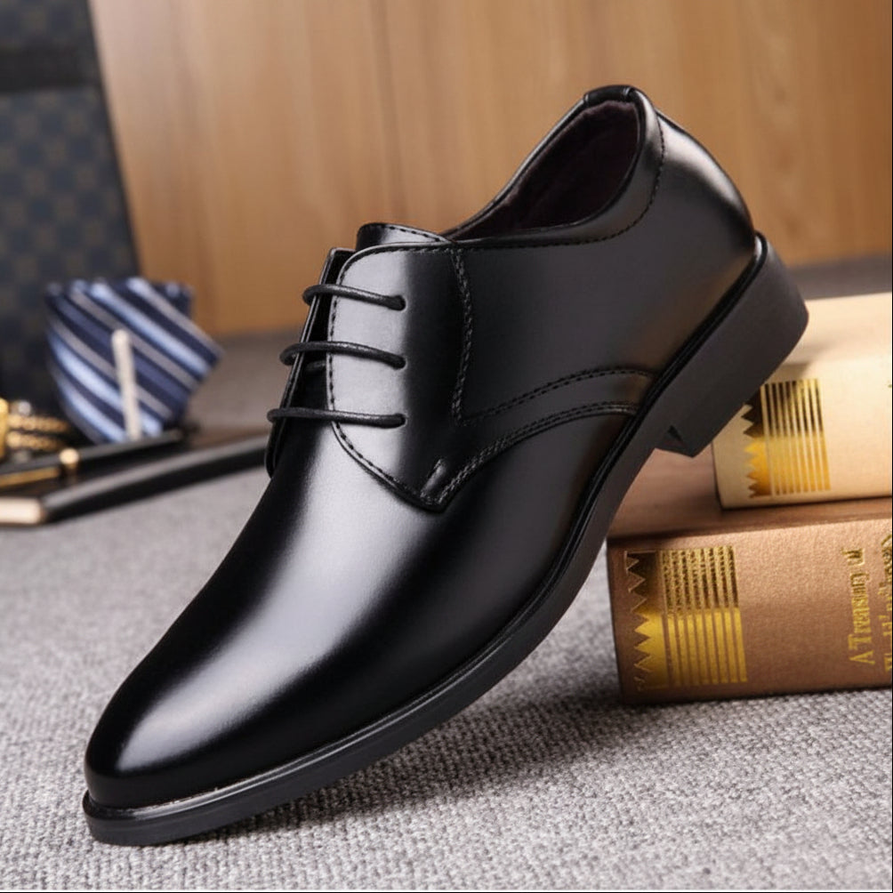 Black dress shoe on a textured surface with books and a striped fabric in the background