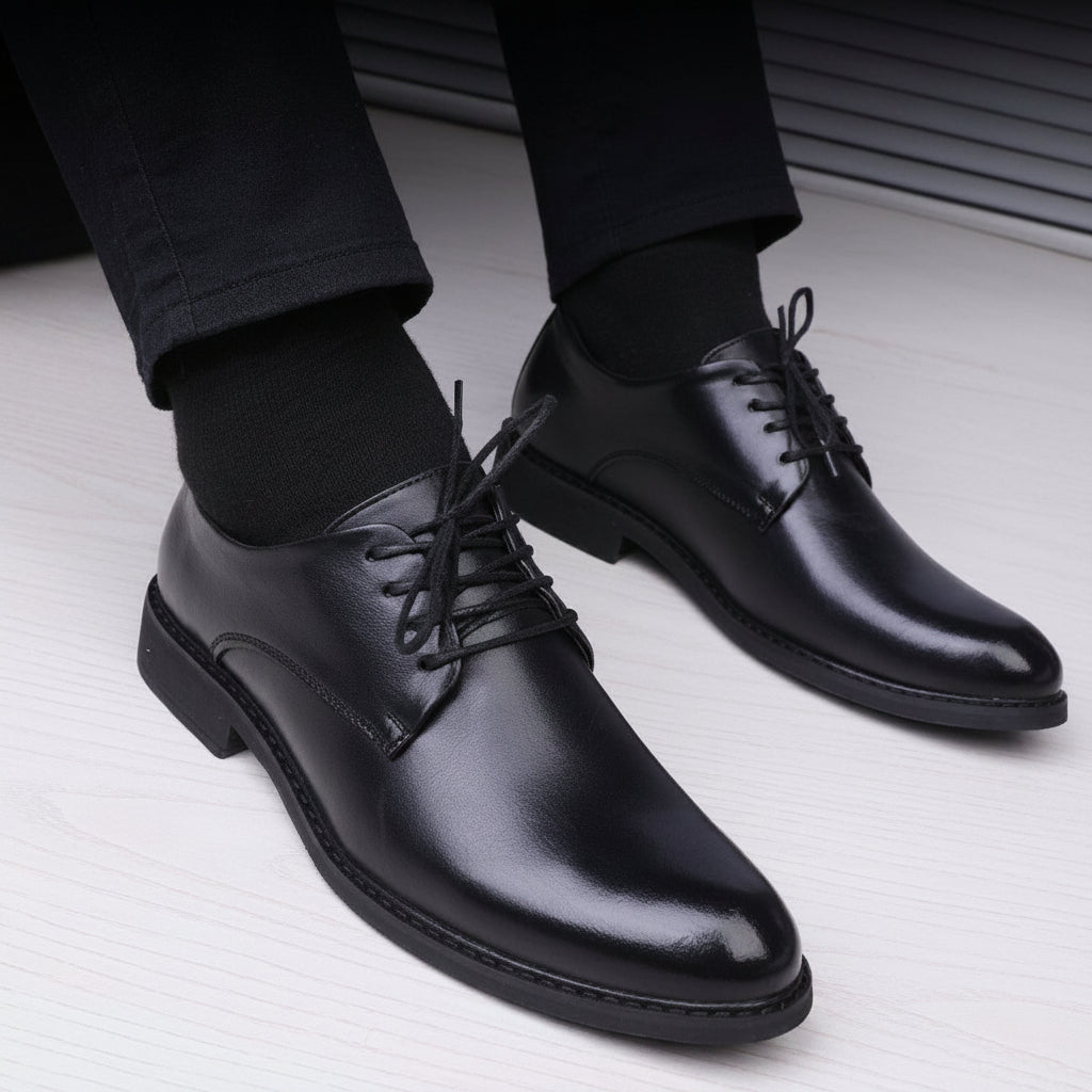 Black leather dress shoes worn with black pants on a light gray floor.