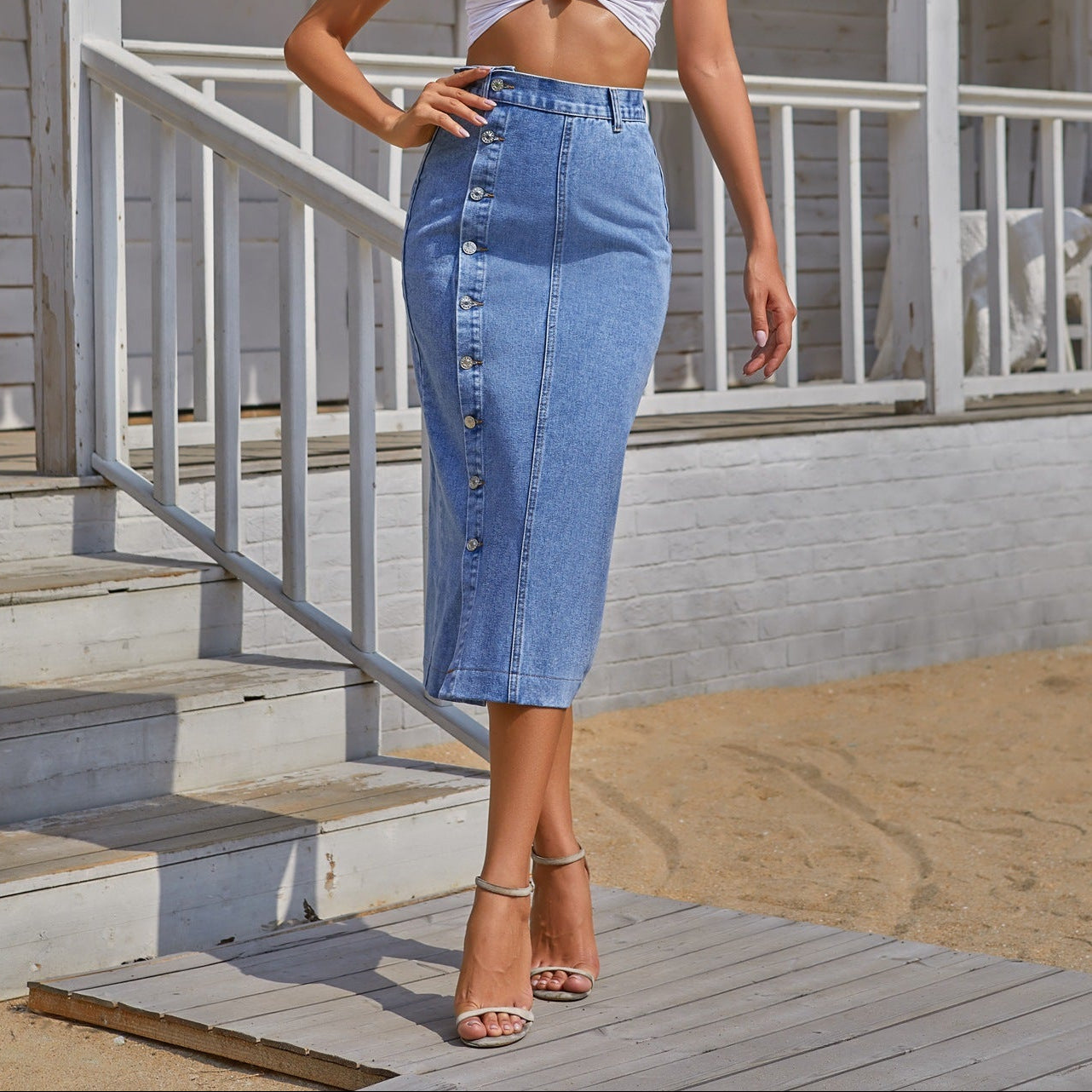 Woman wearing a white crop top and blue denim skirt standing on a wooden deck.