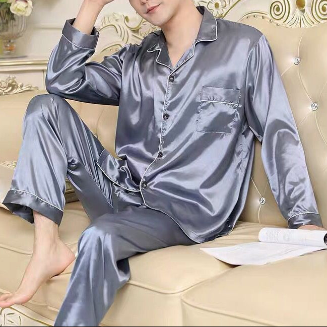 Man wearing gray satin pajamas sitting on a beige couch in a decorated room.