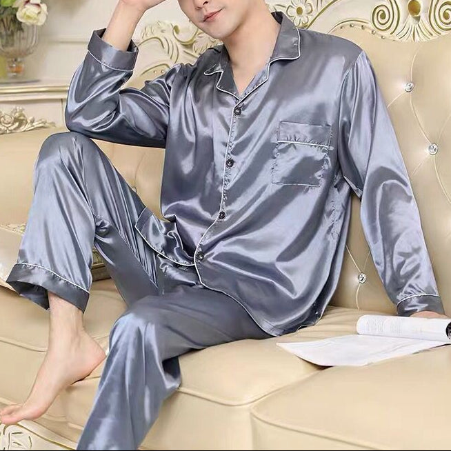 Man wearing gray satin pajamas sitting on a beige couch in a decorated room.