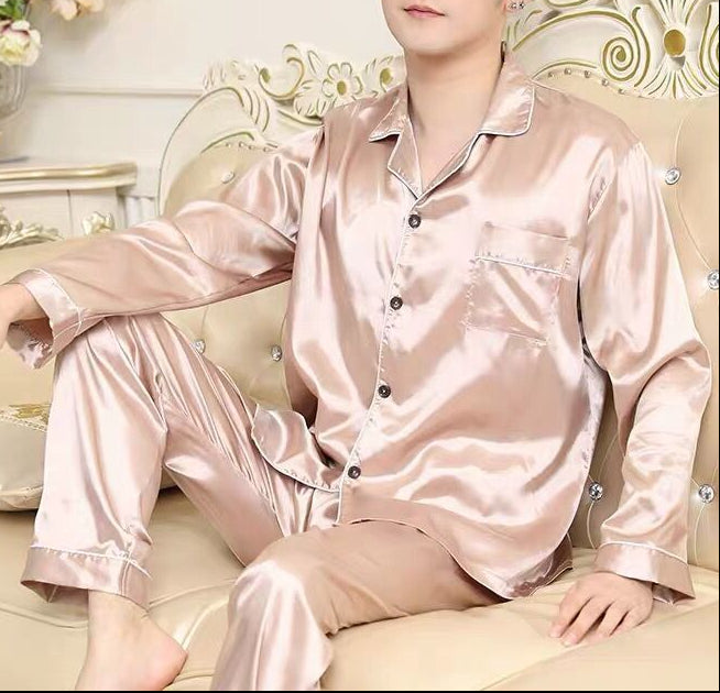 Man wearing pink satin pajamas sitting on a decorative couch with floral arrangements in the background.