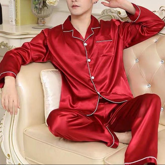 Man wearing red satin pajamas sitting on a beige couch with decorative elements in the background.
