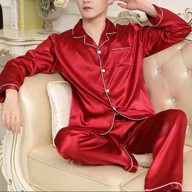 Man wearing red satin pajamas sitting on a beige couch with decorative elements in the background.