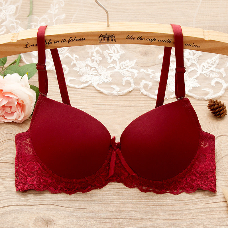 Red bra with lace details on a wooden hanger with floral and pine cone decorations.