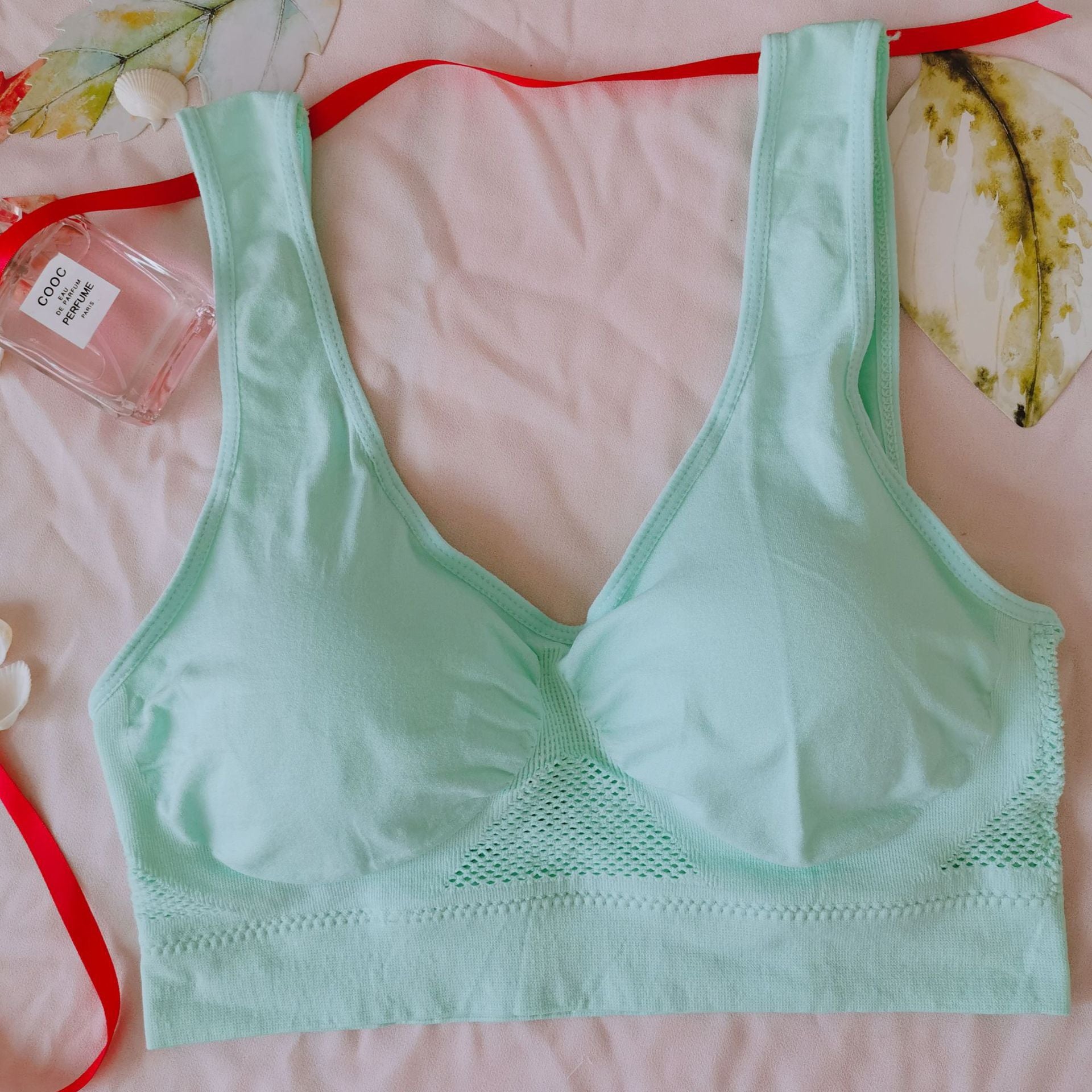 Light green bra on a pink surface with a perfume bottle and decorative elements.