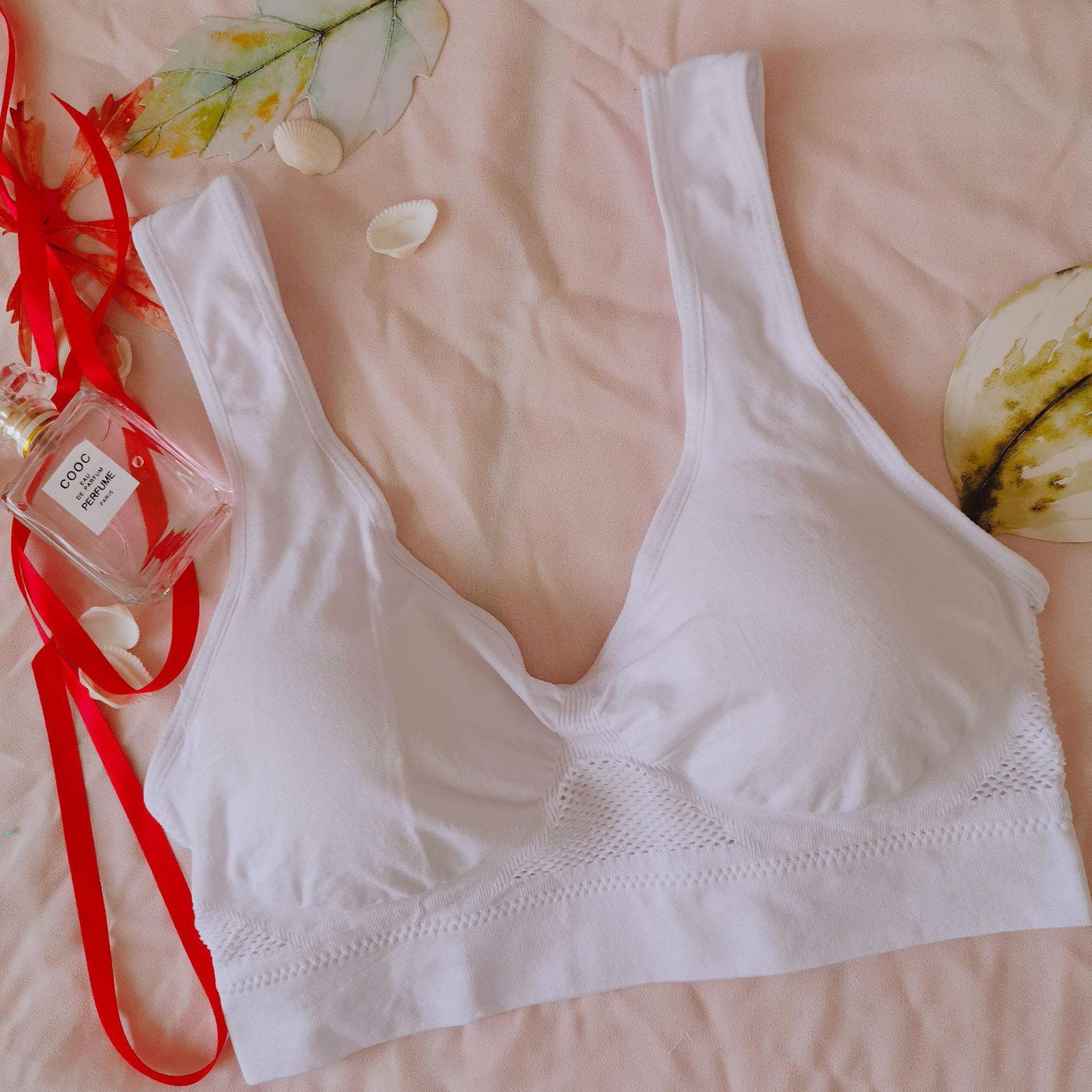White bralette on a pink surface with a small bottle of perfume and red ribbon.