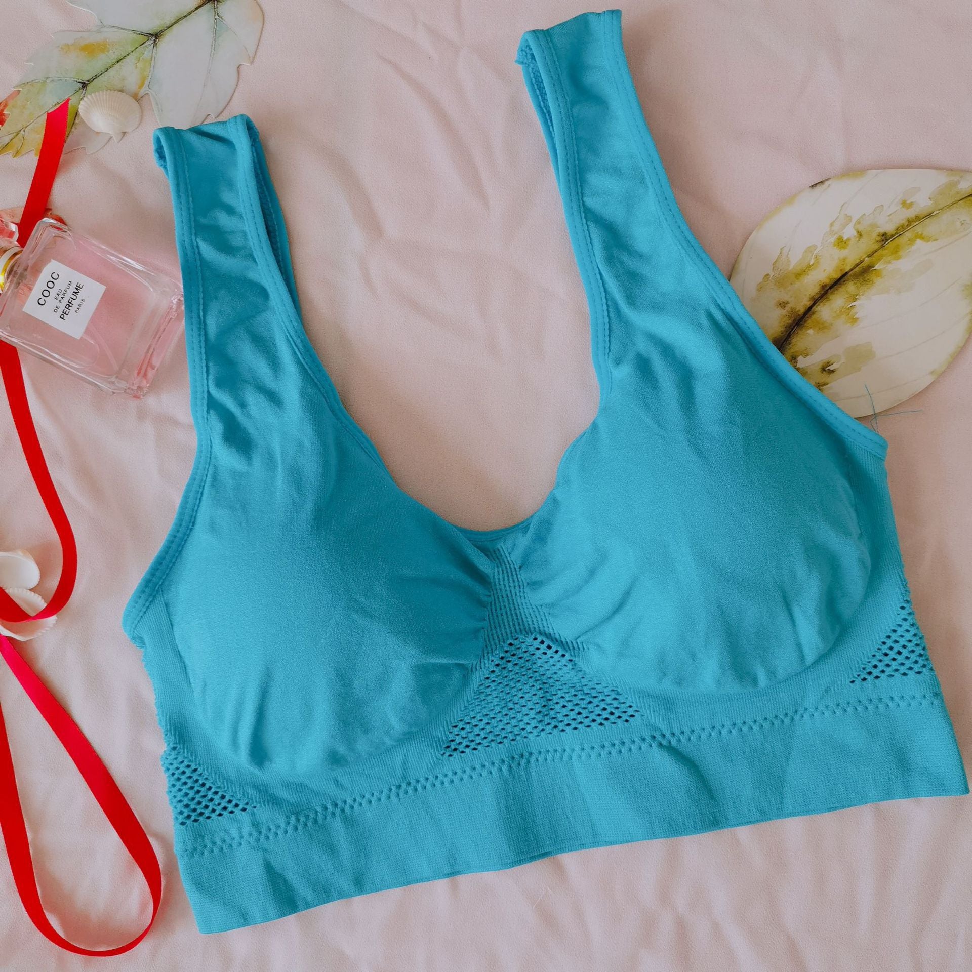 Blue bralette on a pink surface with a red lanyard and small bottle nearby.