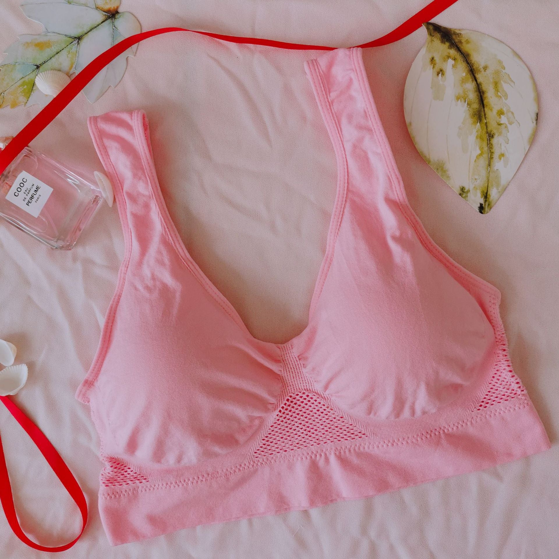 Pink bralette on a light pink surface with a red ribbon and small bottle of perfume.