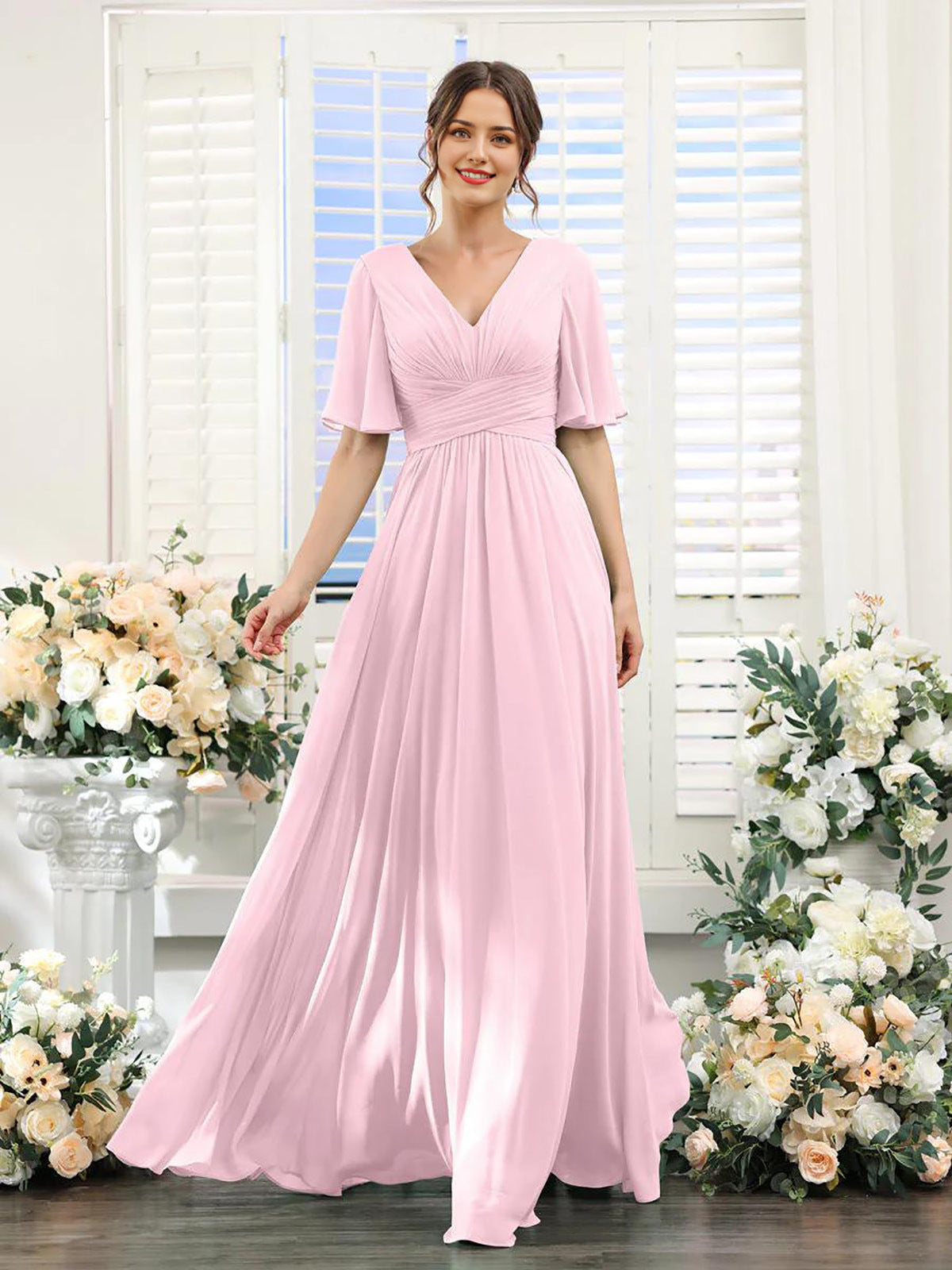 Woman wearing a pink dress standing in front of floral decorations.