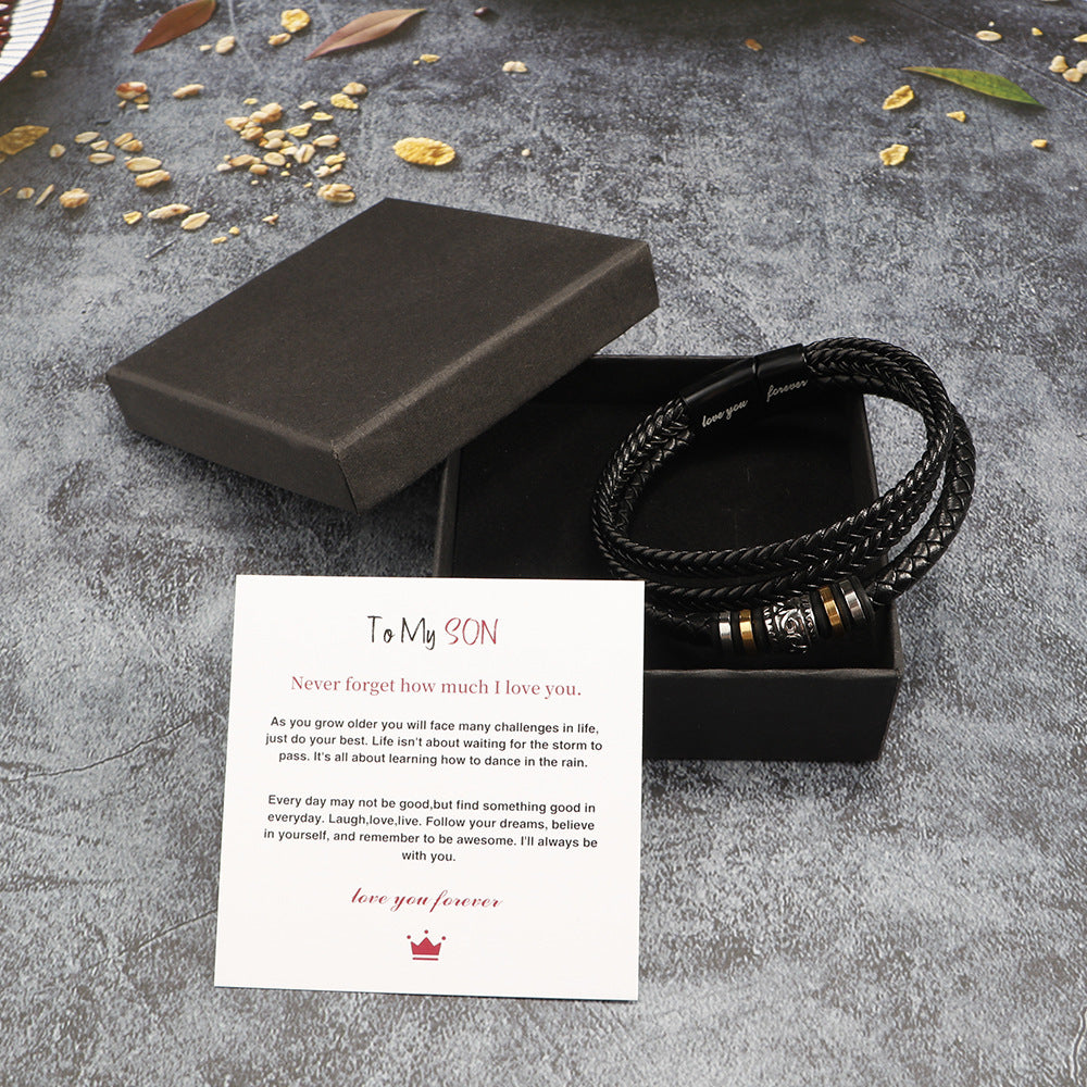 Black braided bracelet with charms on a card in a black box on a textured surface