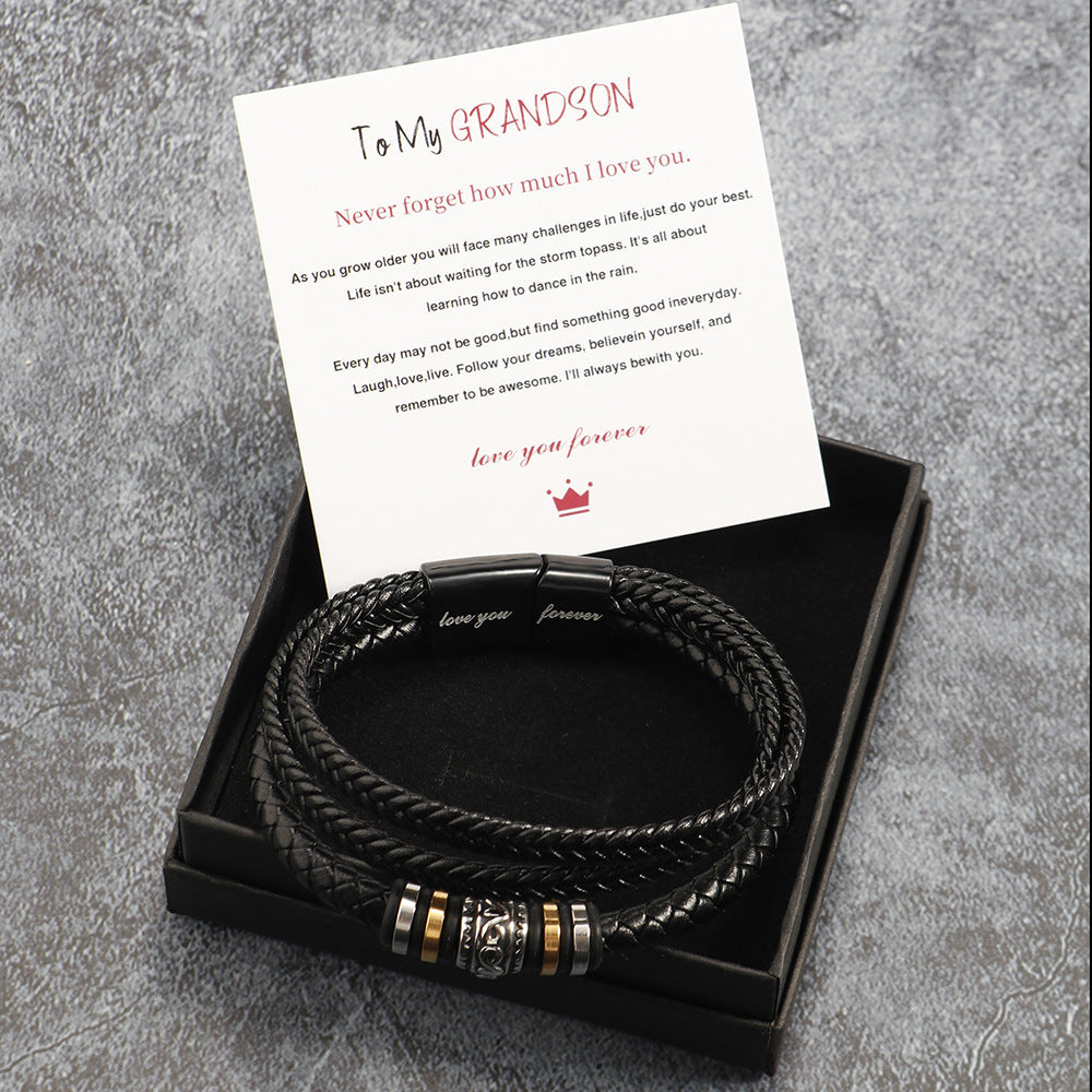 Black braided leather bracelet with gold accents in a box with a card on a gray textured background