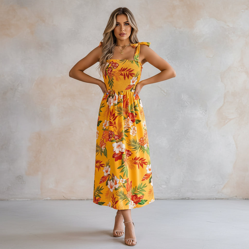 Woman wearing a yellow floral dress in a bright room with a plant and chair.