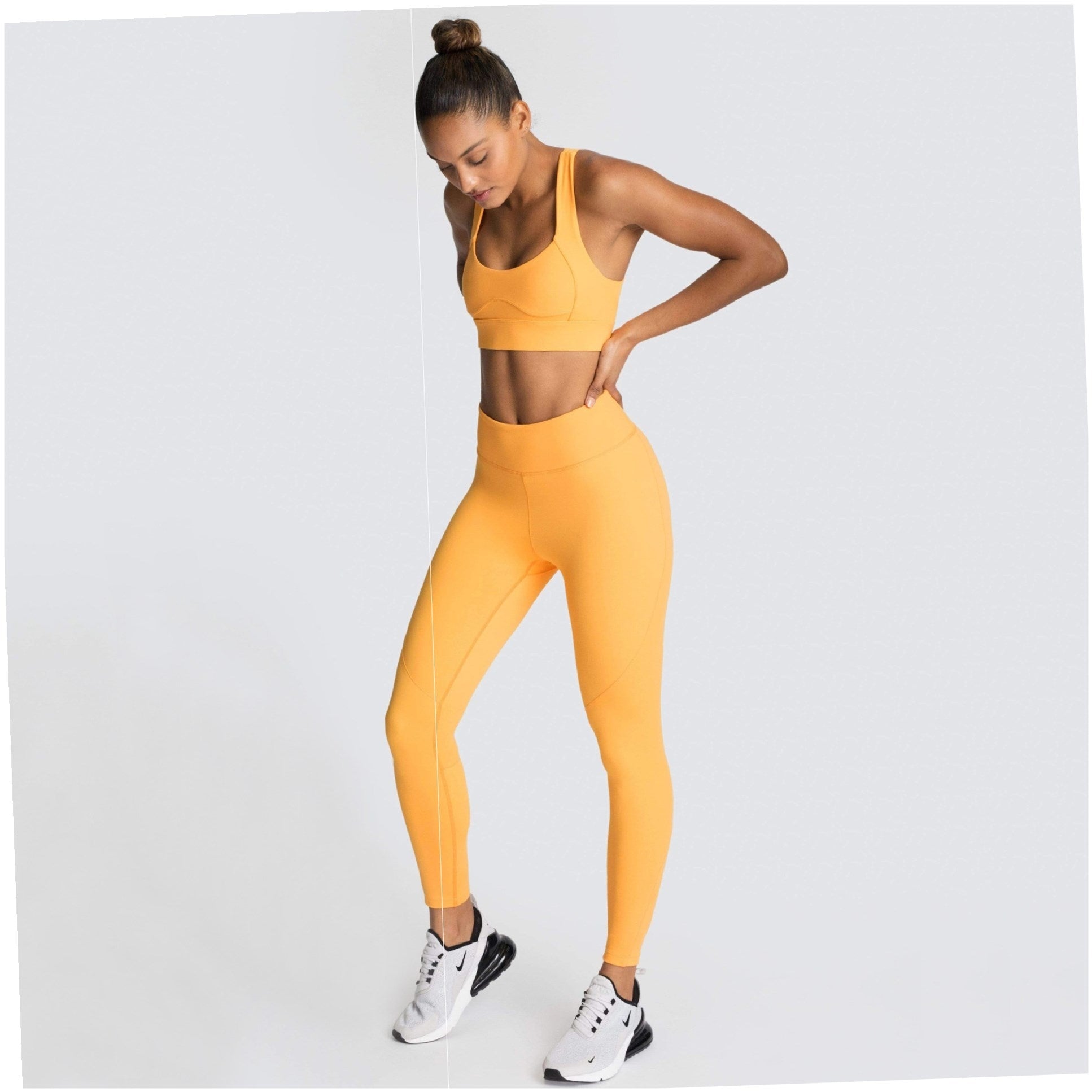 Woman wearing a yellow sports bra and leggings set on a light gray background