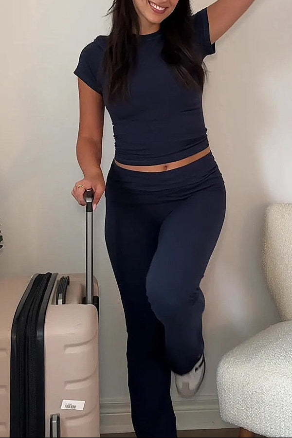 Woman in navy outfit with suitcase against a neutral wall