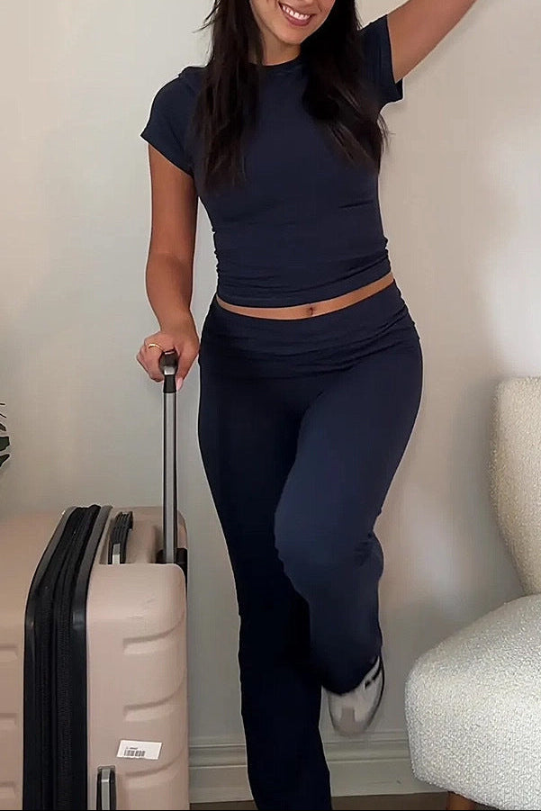 Woman in navy outfit with suitcase against a neutral wall