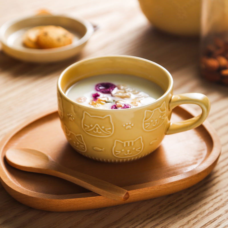 Yellow mug with cat designs on a wooden tray with a spoon, on a wooden table.