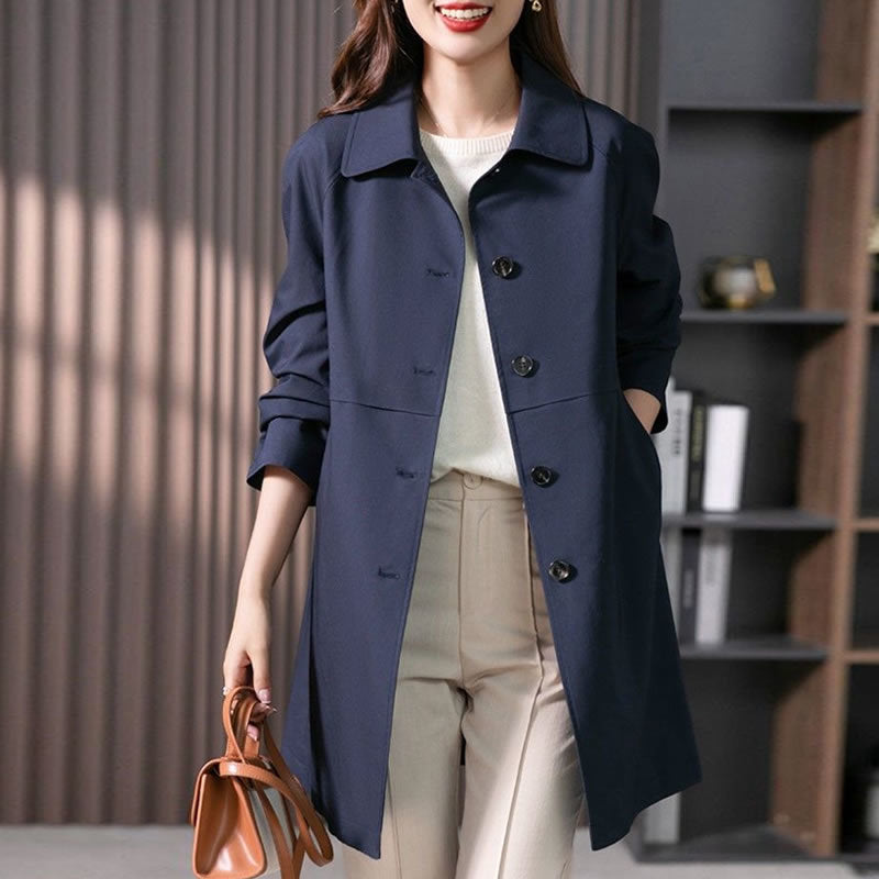Woman wearing a navy blue coat with a white shirt and beige pants, holding a brown leather bag indoors.