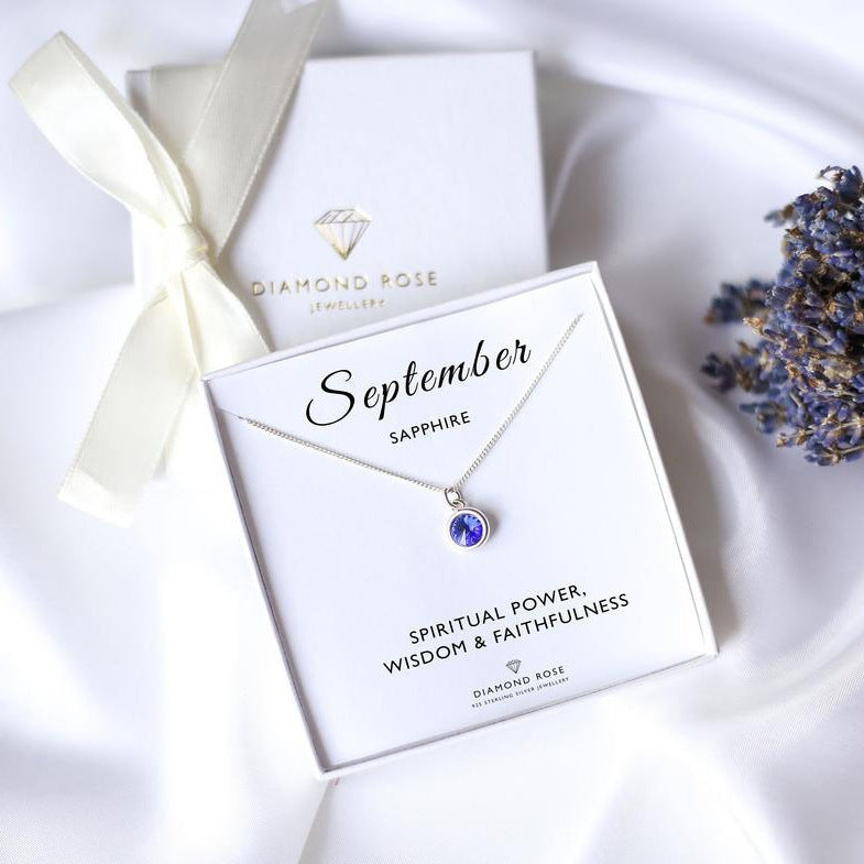 Diamond Rose Jewellery necklace with sapphire pendant on a white box, tied with a ribbon.