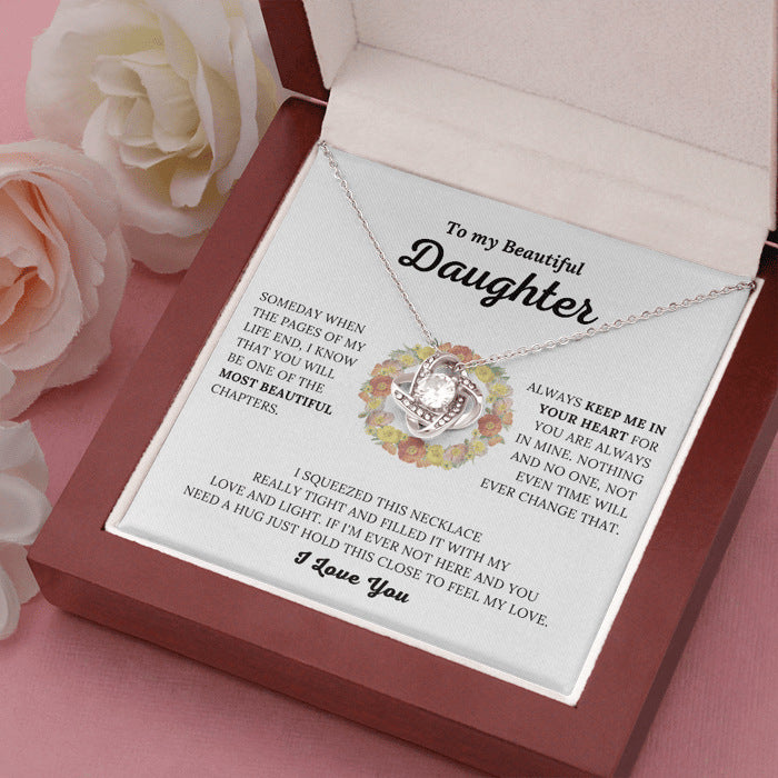 Necklace with floral heart design in a gift box with a sentimental message for a daughter, surrounded by roses.
