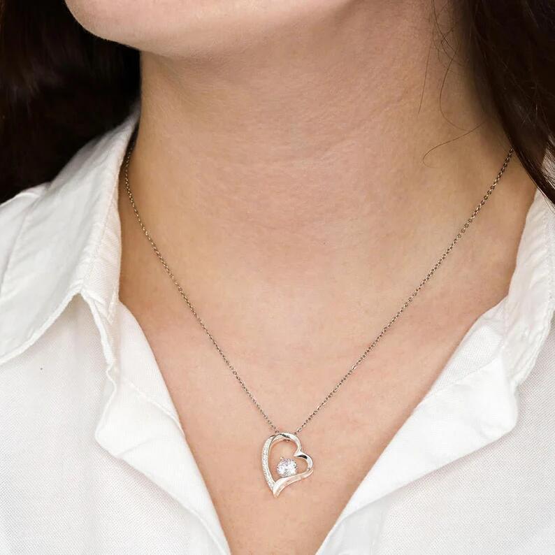 Heart-shaped necklace with a central gemstone worn by a person against a white shirt background