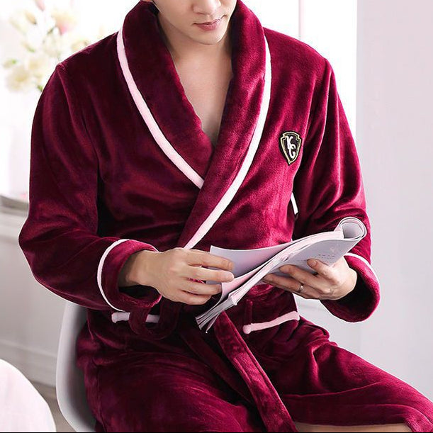 Man wearing a burgundy robe with a white trim, sitting indoors holding a magazine.