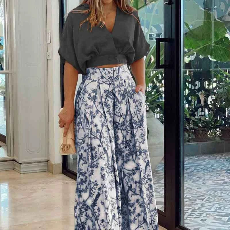 Woman wearing a dark gray top and white floral pants in an indoor setting.