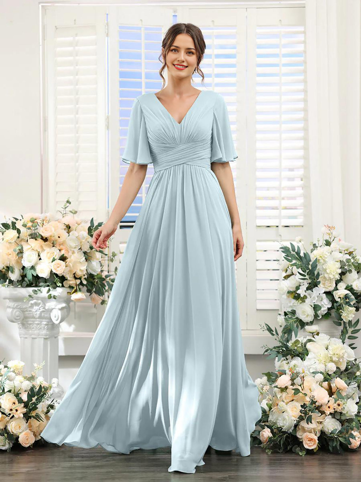 Woman wearing a light blue dress standing in front of floral decorations.