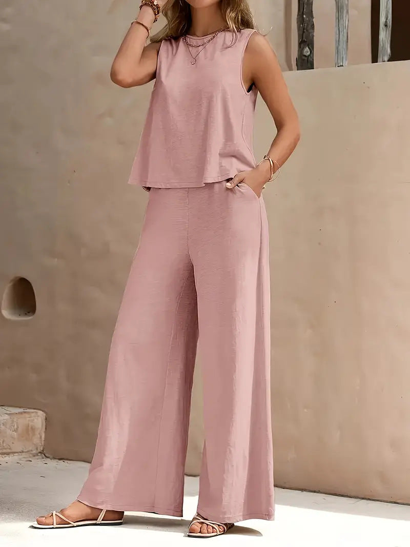 Woman wearing a pink sleeveless top and wide-leg pants against a beige wall.