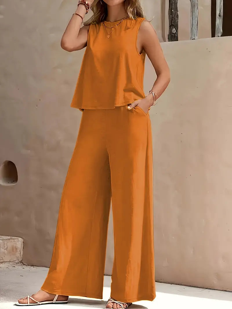 Woman wearing an orange sleeveless top and wide-leg pants against a beige wall.