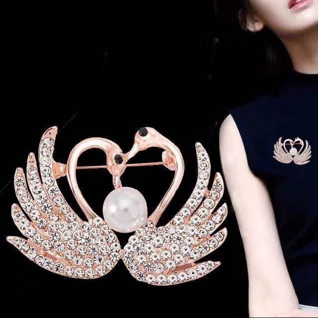 Rose gold brooch with pearl and wings next to a person wearing a black shirt with a similar brooch design.