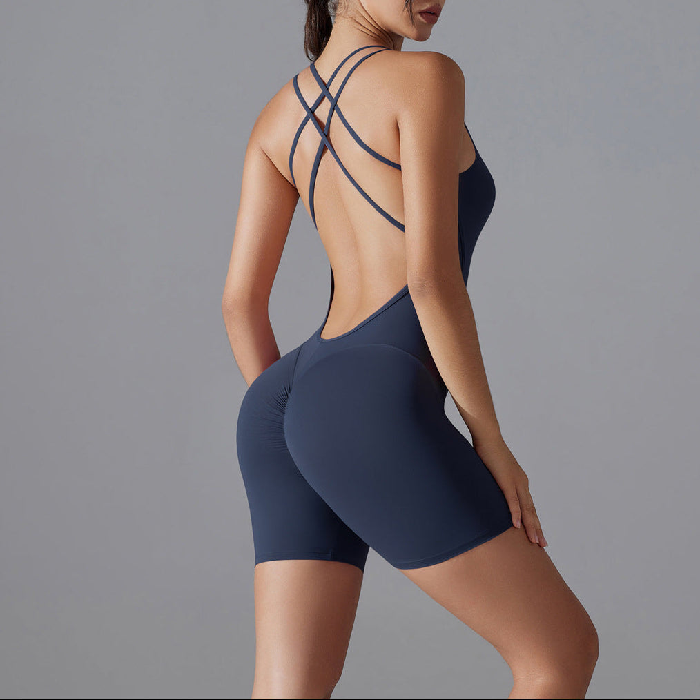 Woman wearing a navy blue swimsuit with criss-cross straps on a gray background