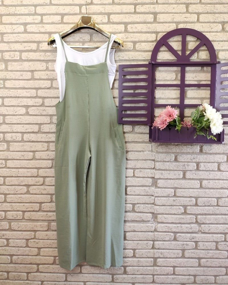 Green jumpsuit on a hanger against a brick wall with a decorative window and flowers.