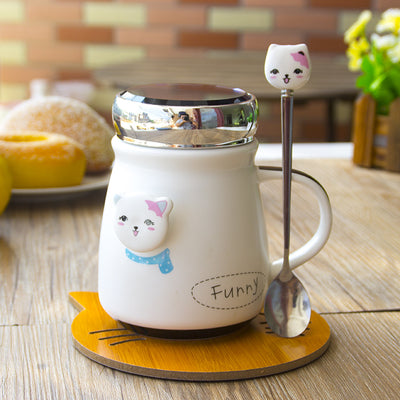 Cute mug with a cat design on a wooden table with a spoon and coaster.