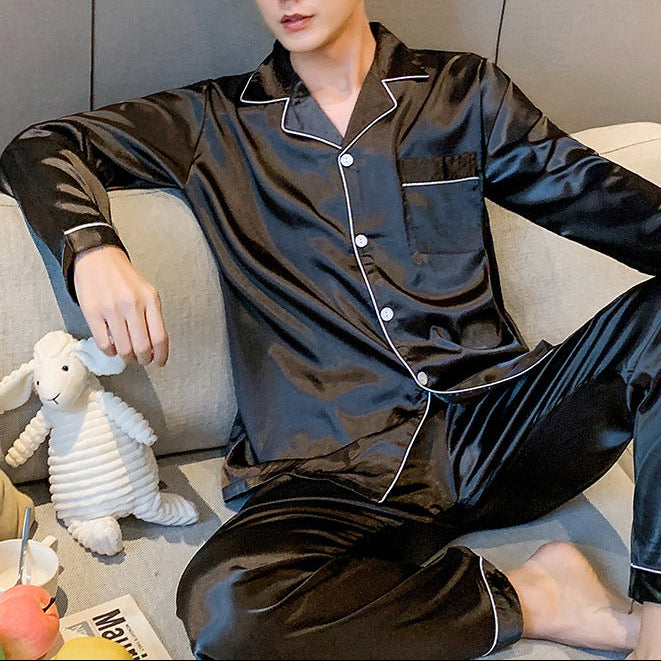 Man wearing black satin pajamas sitting on a couch with a toy sheep and fruit.