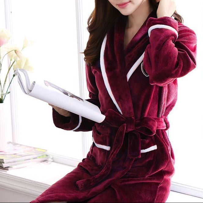 Woman in a burgundy robe holding a book in a bright room with flowers and books on a surface.