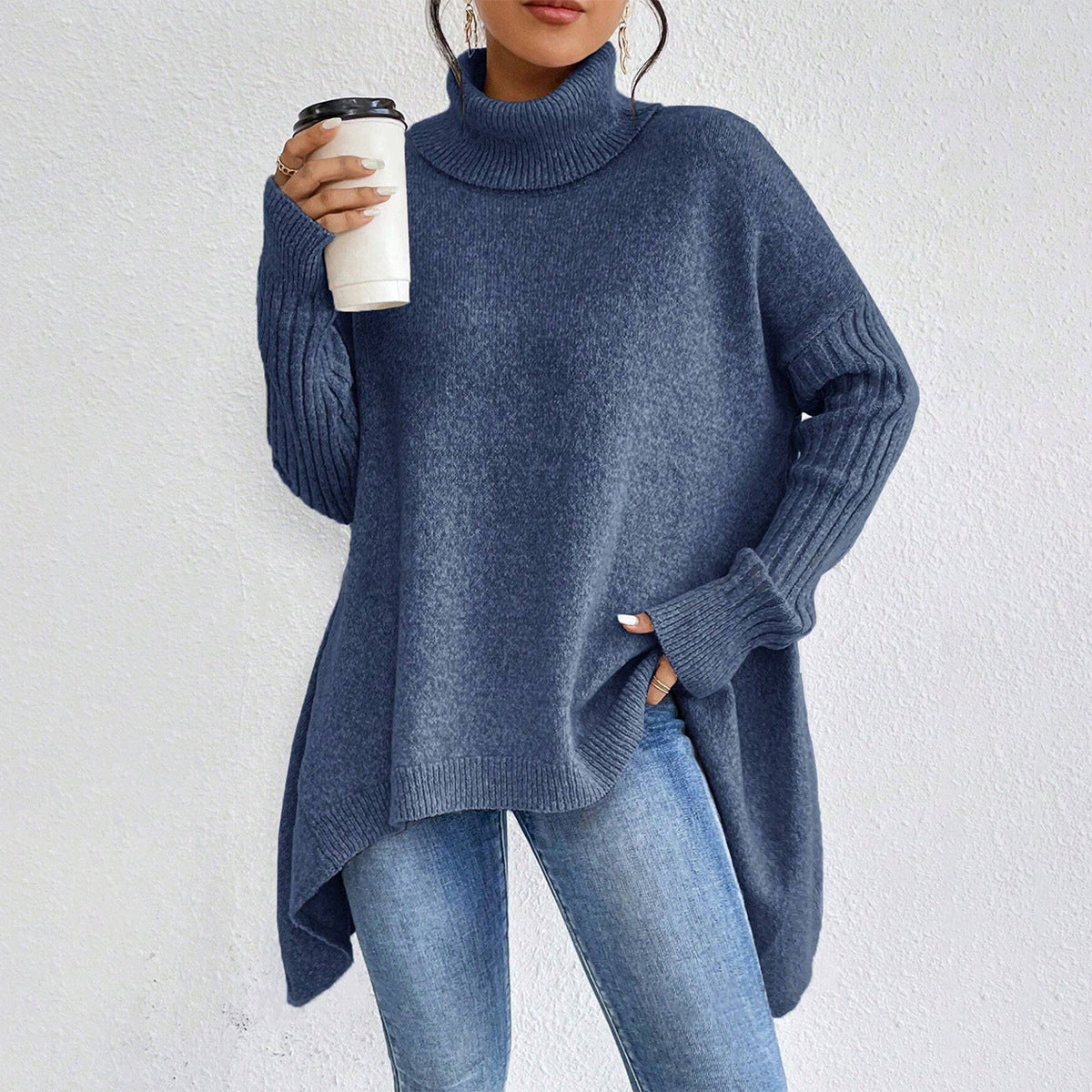 Person wearing a blue sweater and jeans, holding a white cup with a black lid against a light gray background