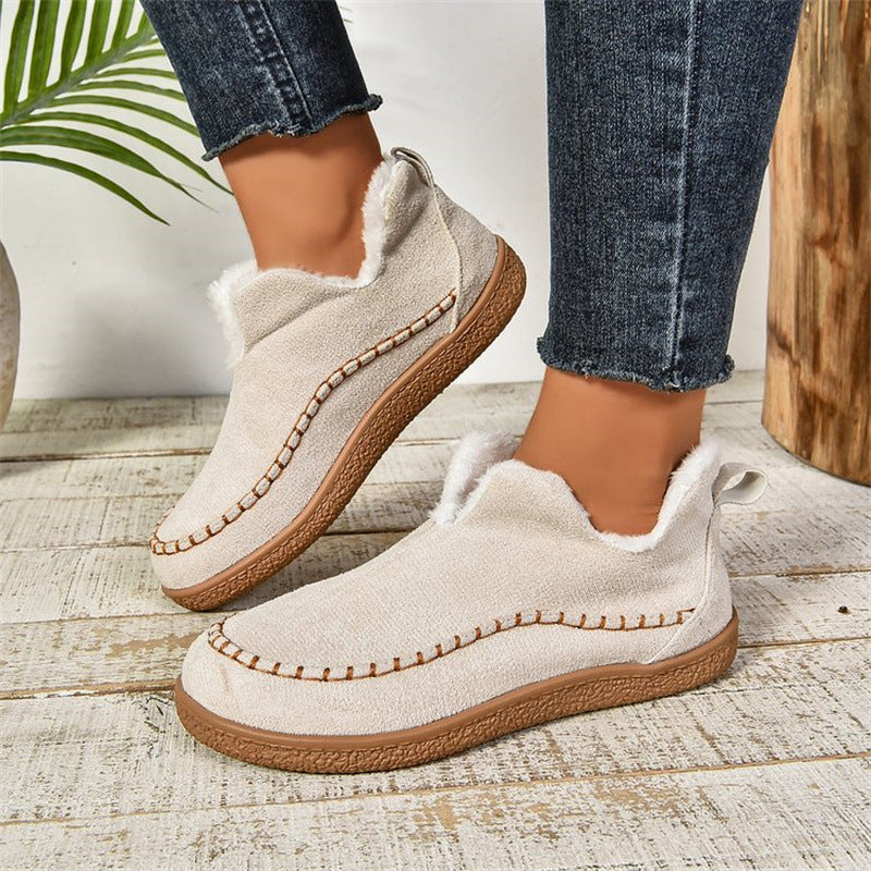 Beige slip-on shoes with brown soles worn indoors on a wooden floor.