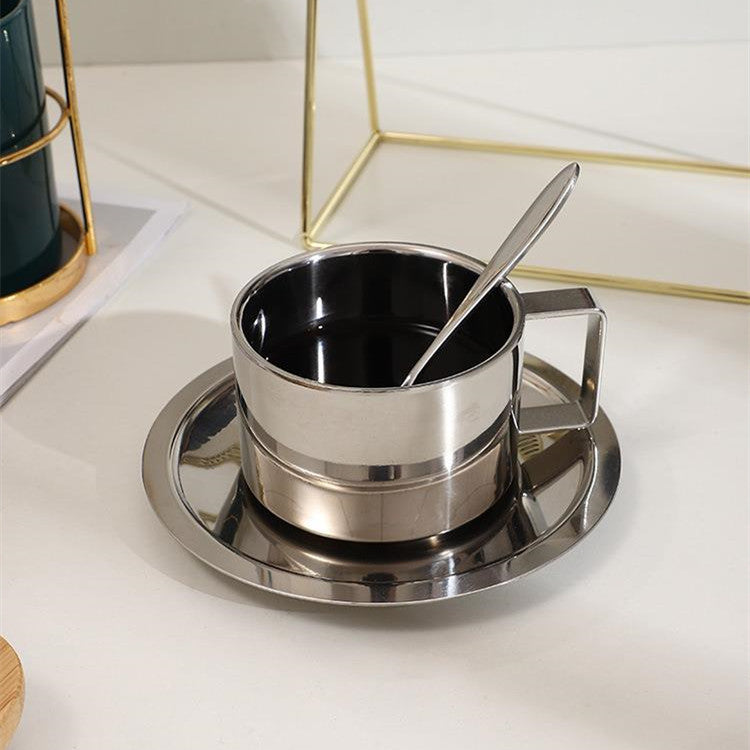 Stainless steel cup with saucer and spoon on a white surface