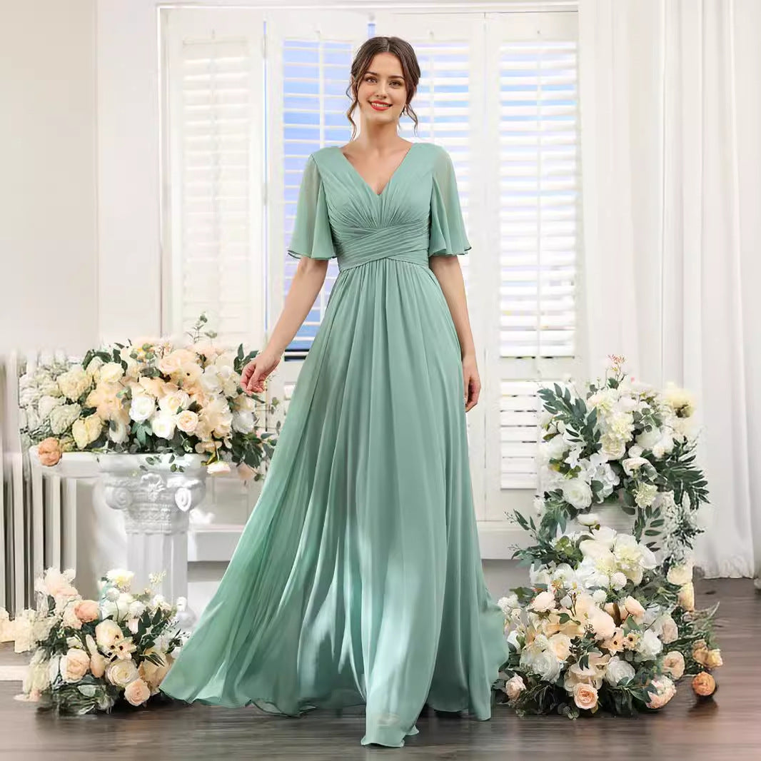 Woman in a long green dress standing in front of floral arrangements indoors.